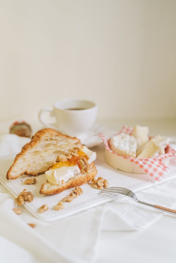 A delicious breakfast scene featuring a croissant with cheese, nuts, and coffee on a light background.