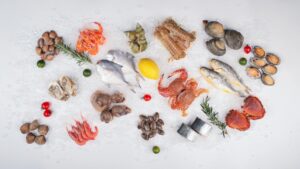 Fresh seafood assortment on ice with lemon, herbs, and vegetables, perfect for culinary uses.