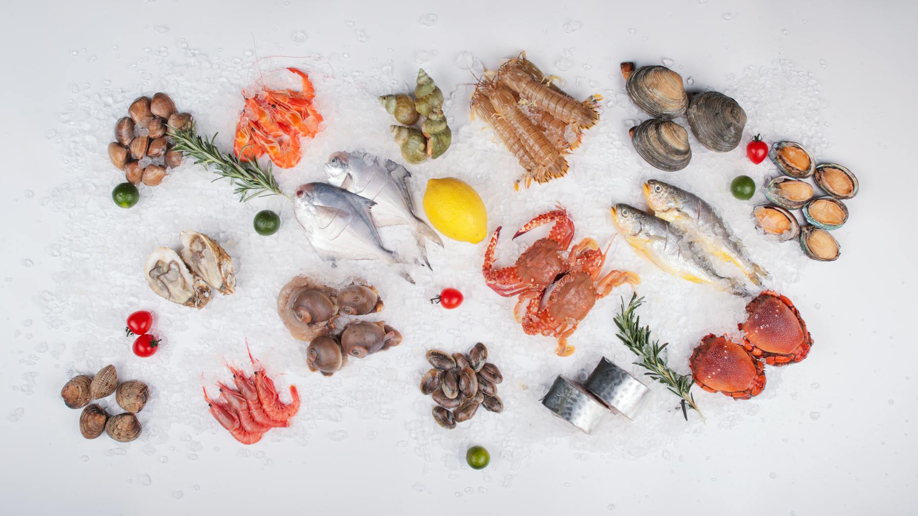 Fresh seafood assortment on ice with lemon, herbs, and vegetables, perfect for culinary uses.
